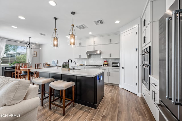 kitchen with white cabinetry, stainless steel appliances, pendant lighting, an island with sink, and hardwood / wood-style floors