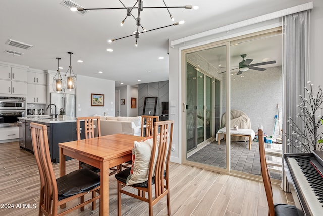 dining space featuring ceiling fan with notable chandelier, sink, and light wood-type flooring