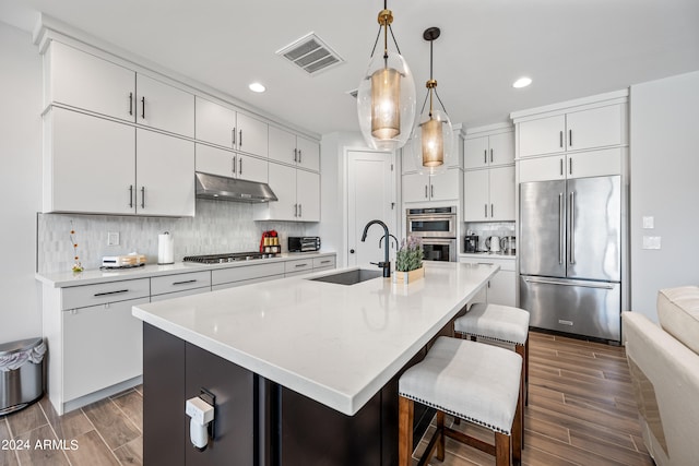 kitchen featuring appliances with stainless steel finishes, a center island with sink, sink, backsplash, and decorative light fixtures