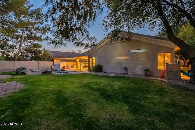 back house at dusk with a yard and a patio