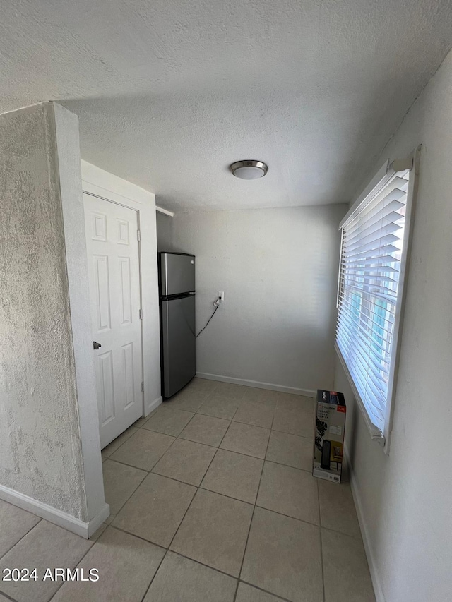 hall with baseboards, a textured ceiling, and light tile patterned flooring