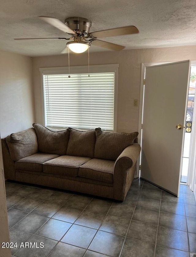 living room with ceiling fan, a textured ceiling, and dark tile patterned floors