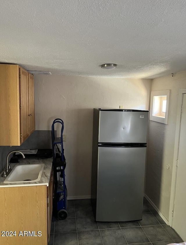 kitchen with a sink, a textured ceiling, freestanding refrigerator, brown cabinets, and light countertops
