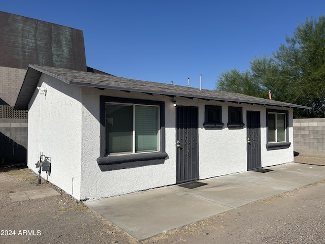 view of front of house featuring a patio, a shingled roof, and stucco siding