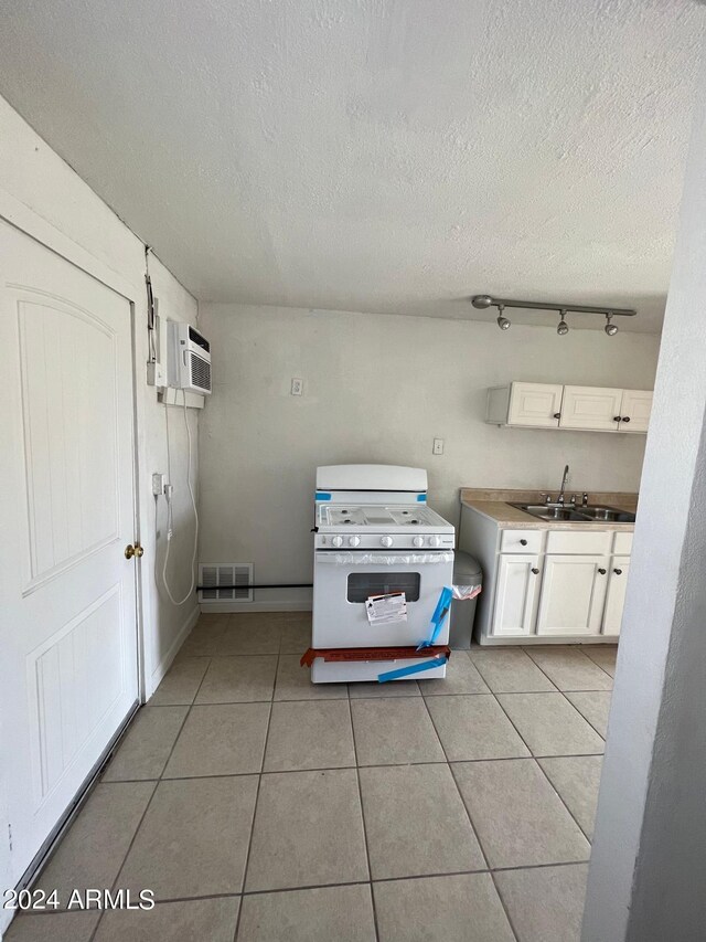 kitchen with light tile patterned floors, a textured ceiling, sink, and white cabinetry