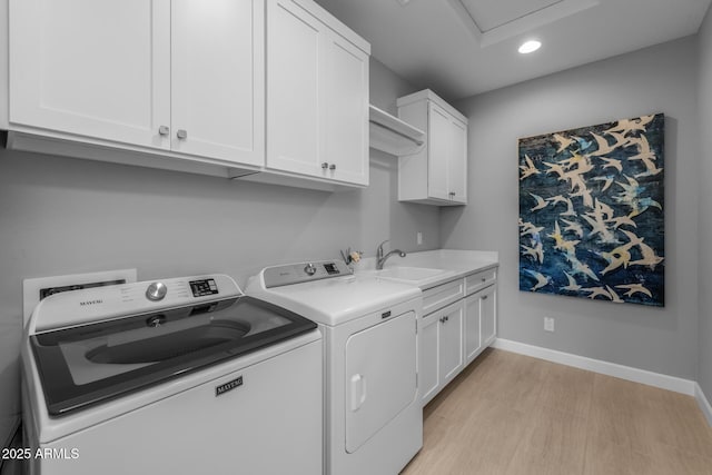 laundry area featuring sink, washing machine and dryer, cabinets, and light wood-type flooring