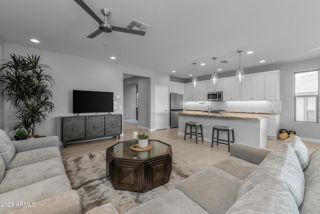 living room featuring ceiling fan, sink, and light hardwood / wood-style floors