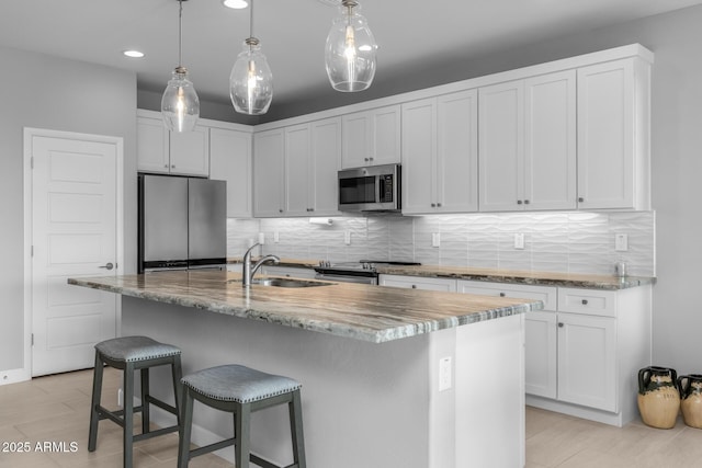 kitchen with appliances with stainless steel finishes, decorative light fixtures, sink, white cabinets, and a center island with sink