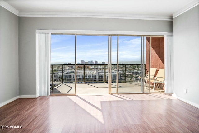 unfurnished room featuring a view of city, crown molding, baseboards, and wood finished floors