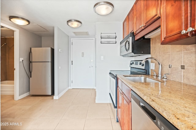 kitchen with light stone counters, light tile patterned flooring, stainless steel appliances, a sink, and decorative backsplash
