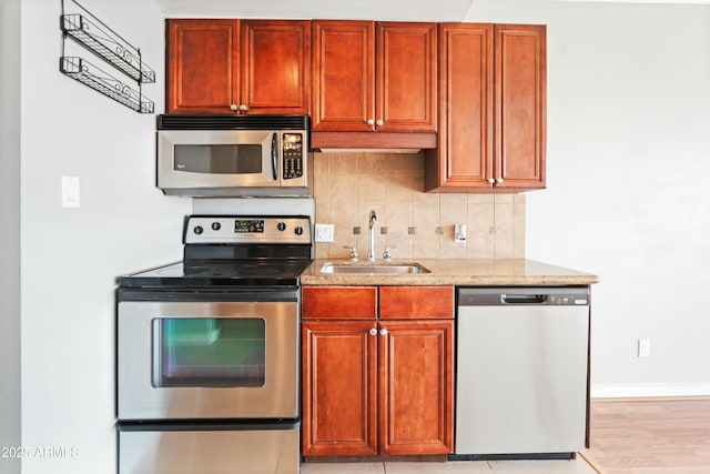 kitchen featuring a sink, baseboards, appliances with stainless steel finishes, backsplash, and light stone countertops