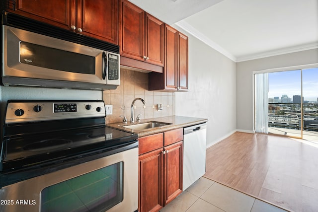 kitchen featuring stainless steel appliances, a sink, baseboards, ornamental molding, and backsplash