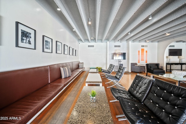 interior space featuring visible vents, beam ceiling, arched walkways, and wood finished floors