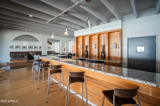 kitchen featuring arched walkways, stone countertops, wood finished floors, a kitchen bar, and pendant lighting