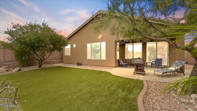 back house at dusk featuring a lawn and a patio