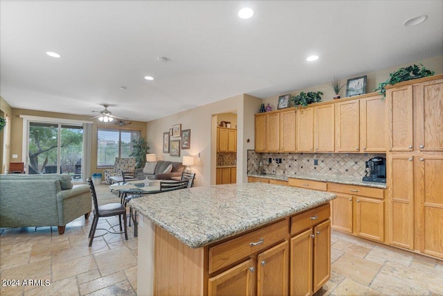 kitchen featuring tasteful backsplash, light stone counters, a center island, and ceiling fan