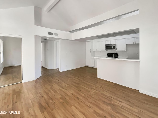 unfurnished living room with hardwood / wood-style floors, beam ceiling, sink, and high vaulted ceiling