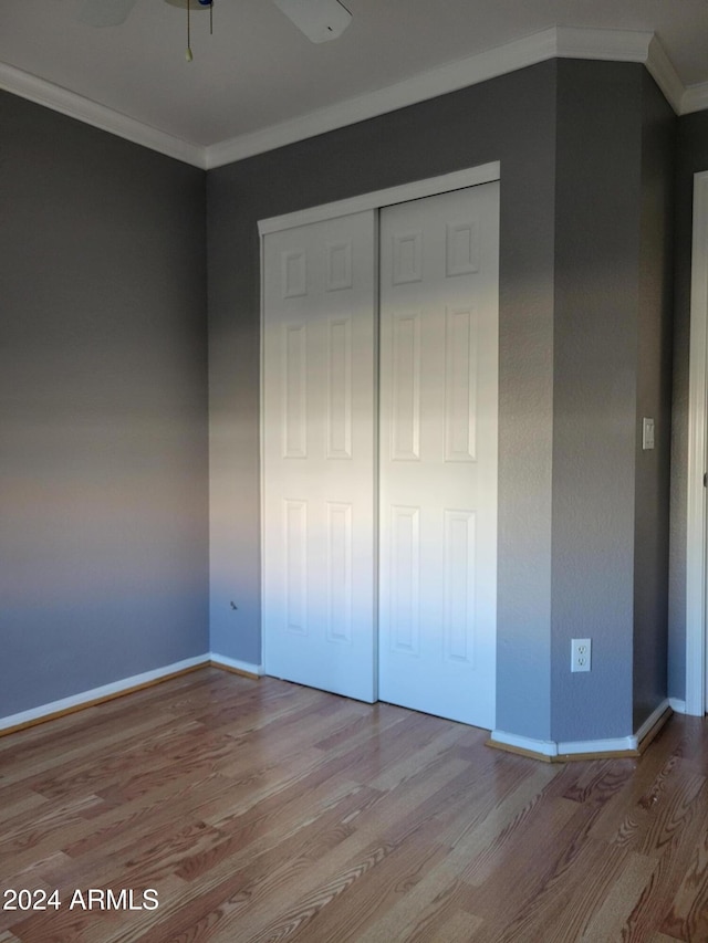 unfurnished bedroom with a closet, crown molding, baseboards, and wood finished floors