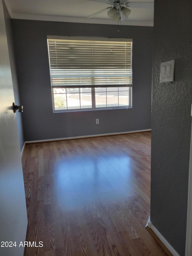 spare room featuring ceiling fan, baseboards, wood finished floors, and crown molding