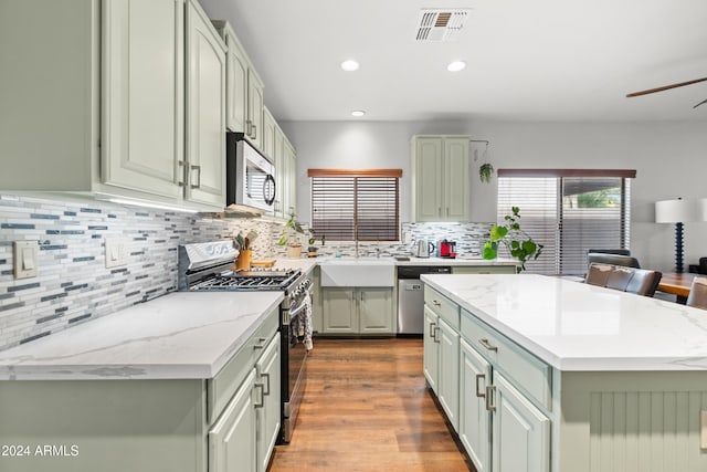 kitchen with decorative backsplash, appliances with stainless steel finishes, light stone counters, light hardwood / wood-style flooring, and a kitchen island