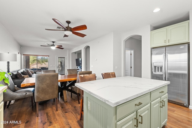 kitchen featuring ceiling fan, green cabinets, stainless steel fridge with ice dispenser, wood-type flooring, and a kitchen island