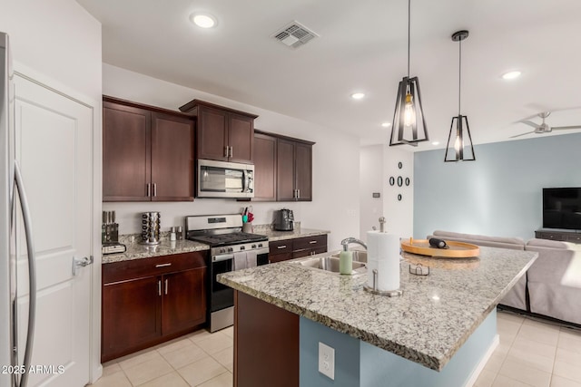 kitchen with sink, appliances with stainless steel finishes, a kitchen island with sink, and hanging light fixtures