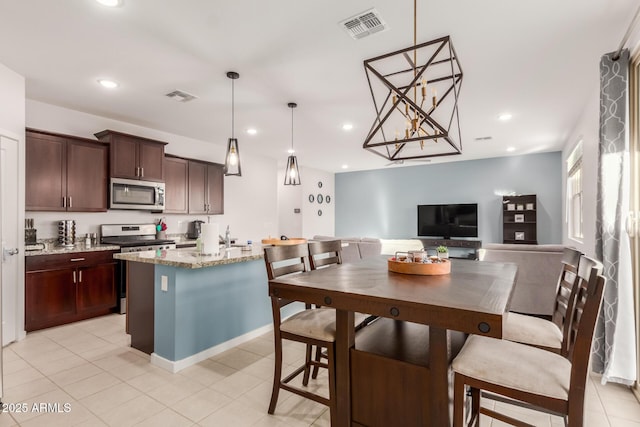 kitchen featuring stainless steel appliances, light stone counters, dark brown cabinets, hanging light fixtures, and a kitchen island with sink