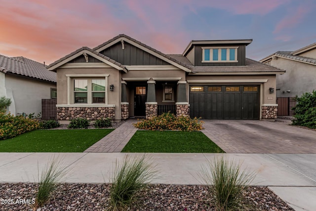craftsman house featuring stone siding, decorative driveway, a front lawn, stucco siding, and a tile roof