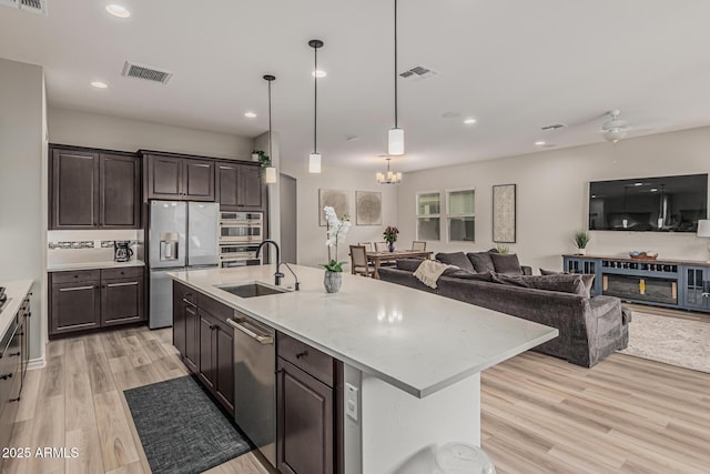 kitchen with stainless steel appliances, a sink, light wood finished floors, dark brown cabinets, and recessed lighting
