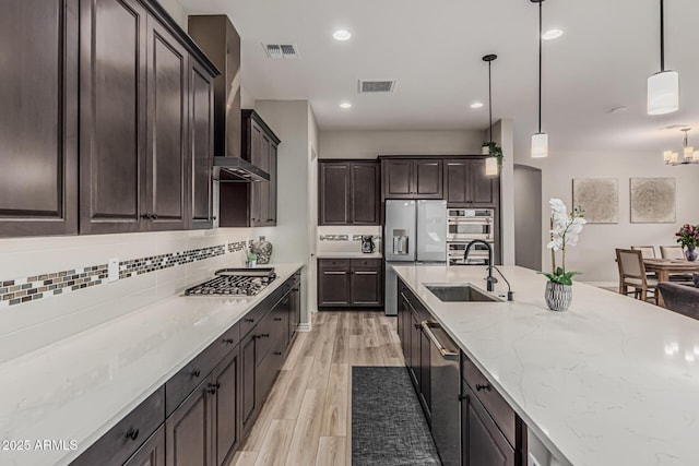 kitchen with appliances with stainless steel finishes, a sink, decorative backsplash, light stone counters, and light wood finished floors