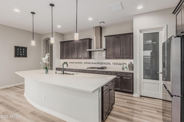 kitchen featuring appliances with stainless steel finishes, wall chimney range hood, a sink, dark brown cabinetry, and recessed lighting