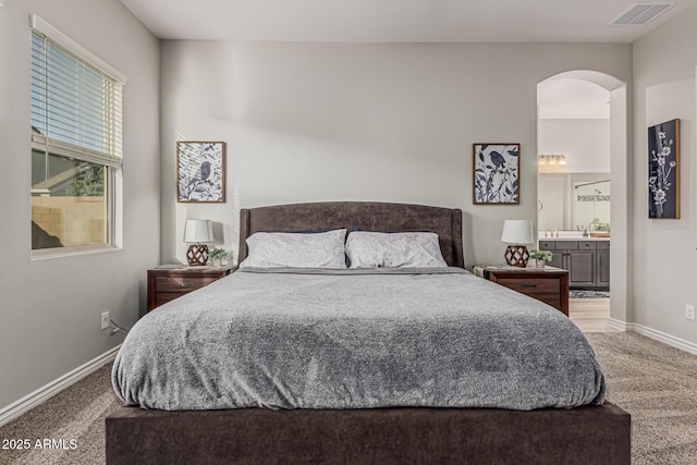 carpeted bedroom featuring baseboards, ensuite bathroom, and arched walkways