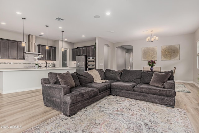 living area featuring arched walkways, light wood-style flooring, a chandelier, baseboards, and recessed lighting