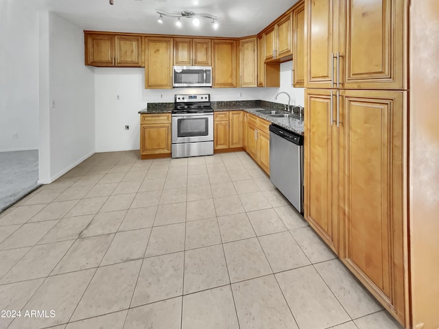 kitchen featuring sink, light tile patterned flooring, dark stone counters, and appliances with stainless steel finishes