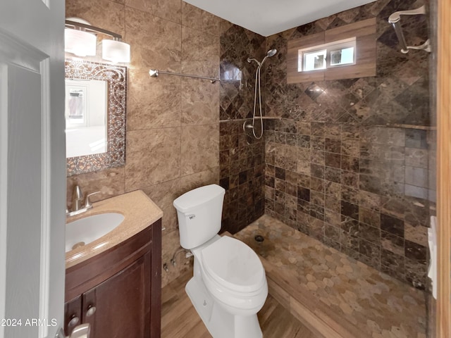 bathroom with a tile shower, vanity, toilet, and tile walls