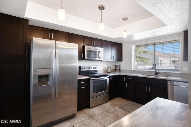 kitchen with sink, light tile patterned floors, hanging light fixtures, stainless steel appliances, and a tray ceiling