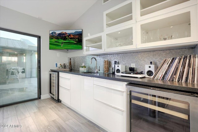 kitchen with white cabinets, vaulted ceiling, sink, and beverage cooler