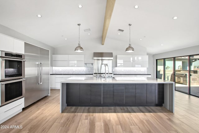 kitchen with appliances with stainless steel finishes, white cabinets, vaulted ceiling with beams, and pendant lighting