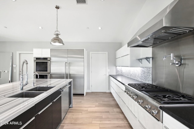 kitchen featuring white cabinets, light hardwood / wood-style flooring, wall chimney exhaust hood, decorative light fixtures, and stainless steel appliances