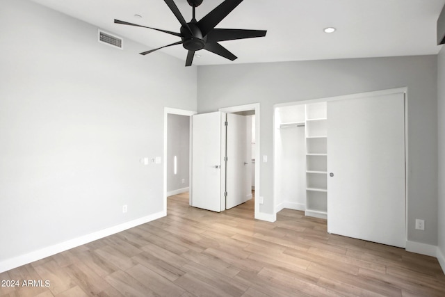 unfurnished bedroom with lofted ceiling, a closet, a walk in closet, light wood-type flooring, and ceiling fan