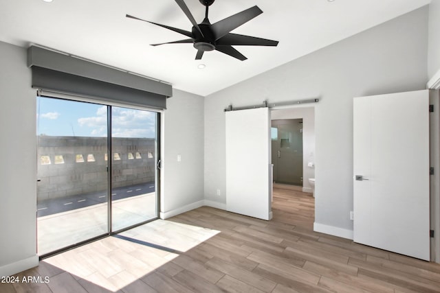 unfurnished room with a barn door, ceiling fan, light wood-type flooring, and vaulted ceiling