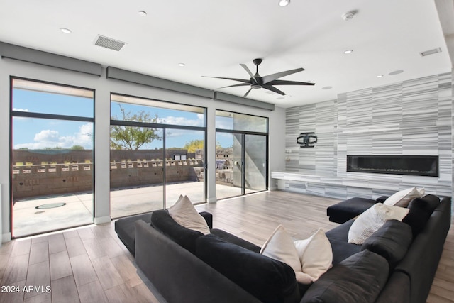 living room featuring light hardwood / wood-style flooring, a large fireplace, tile walls, and ceiling fan