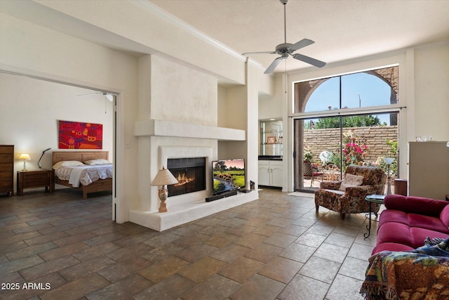 4015 N 78th St Unit 135, Scottsdale, AZ 85251 - living room featuring ceiling fan, a warm lit fireplace, ornamental molding, stone tile flooring, and a towering ceiling