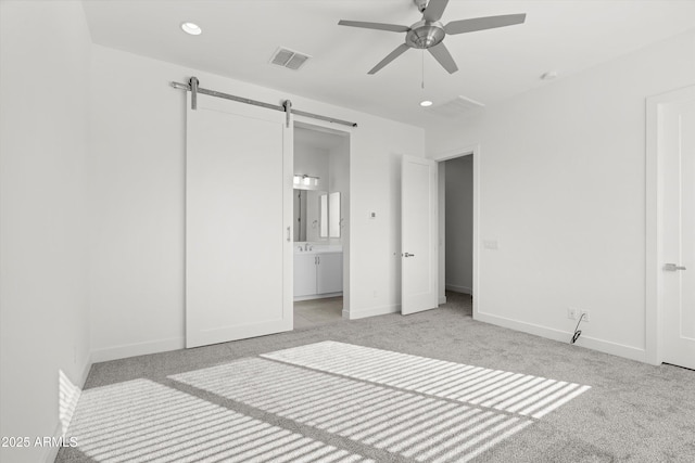 unfurnished bedroom with ceiling fan, ensuite bathroom, a barn door, and light carpet