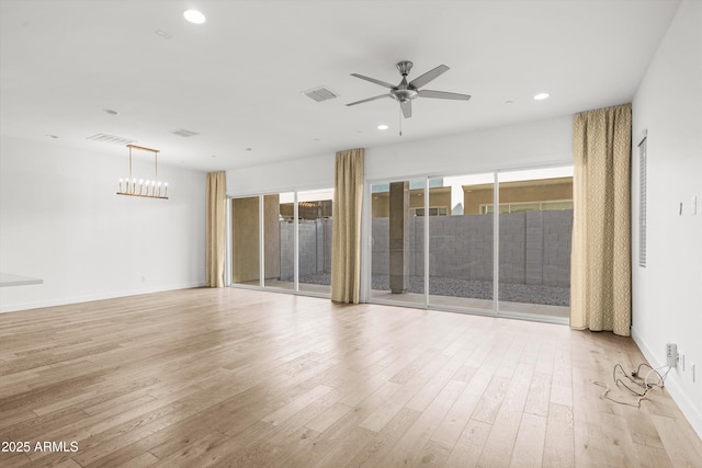 empty room with ceiling fan with notable chandelier and light hardwood / wood-style floors