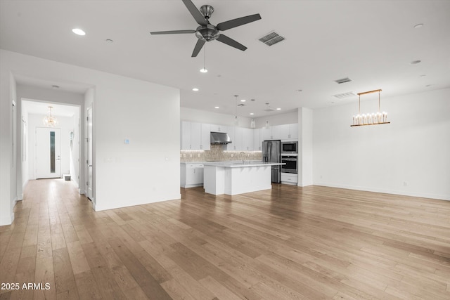 unfurnished living room featuring ceiling fan with notable chandelier and light wood-type flooring