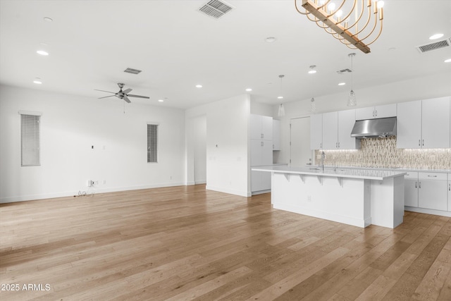 kitchen featuring an island with sink, white cabinets, a kitchen breakfast bar, and decorative backsplash