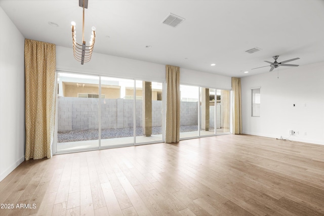 spare room with ceiling fan with notable chandelier and light hardwood / wood-style floors