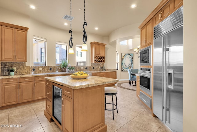 kitchen featuring a kitchen island, decorative light fixtures, tasteful backsplash, wine cooler, and built in appliances