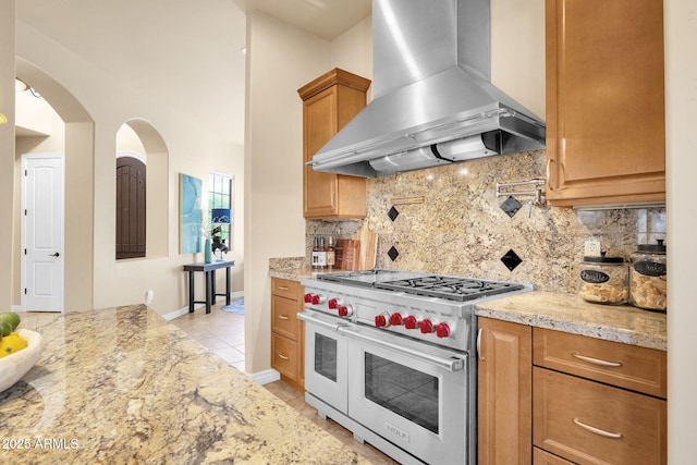 kitchen with range with two ovens, light stone counters, island range hood, light tile patterned floors, and decorative backsplash